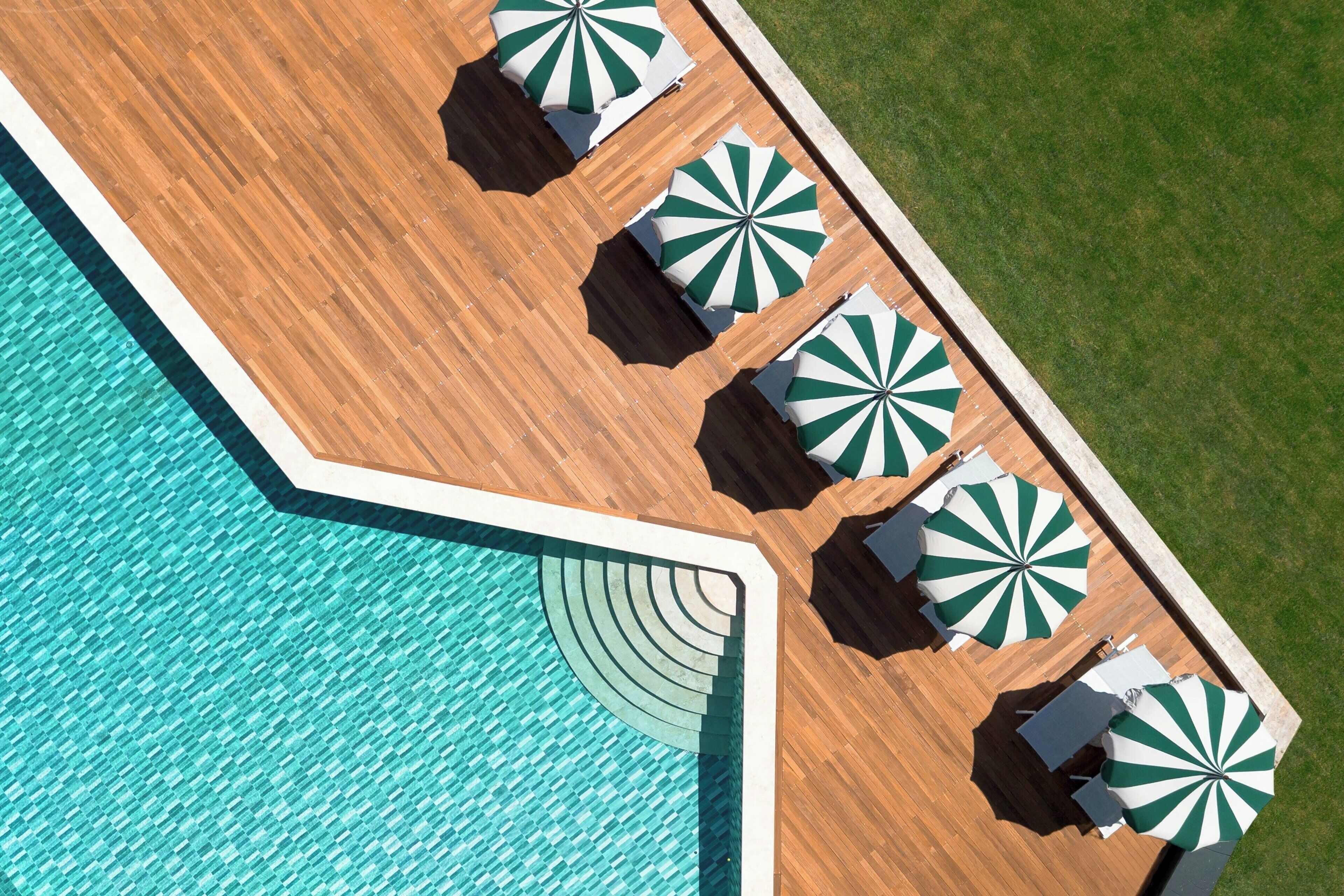 Vista aèria d'una zona de piscina amb terrassa de fusta, una piscina i diverses ombrel·les verdes i blanques a ratlles.