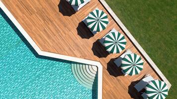 Vista aèria d'una zona de piscina amb terrassa de fusta, una piscina i diverses ombrel·les verdes i blanques a ratlles.