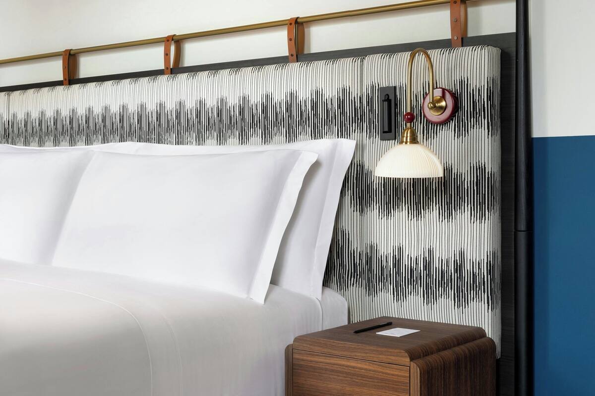 A bed with white linens, a wooden bedside table, and a wall with a striped pattern.