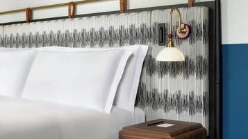 A bed with white linens, a wooden bedside table, and a wall with a striped pattern.