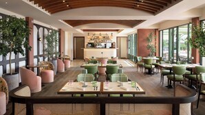 A spacious indoor dining area with wooden ceiling beams, green and pink upholstered chairs, and a central bar area.