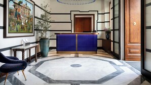 A lobby with a reception desk, a large painting, a potted plant, and a patterned floor.
