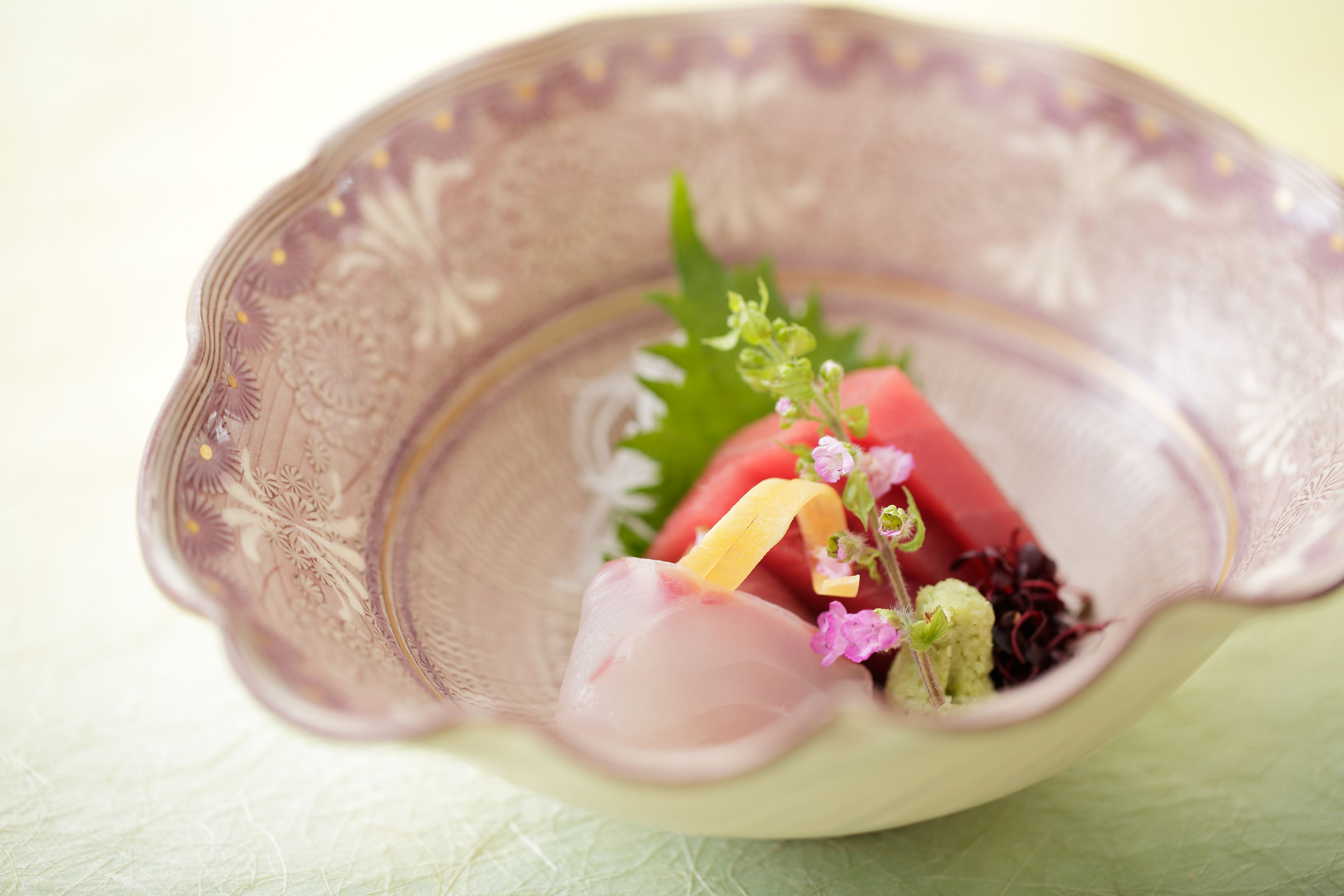 A bowl with a decorative pattern, containing a slice of watermelon, a piece of cucumber, and some greens.