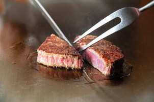Un steak est coupé à l’aide de pinces sur un gril.