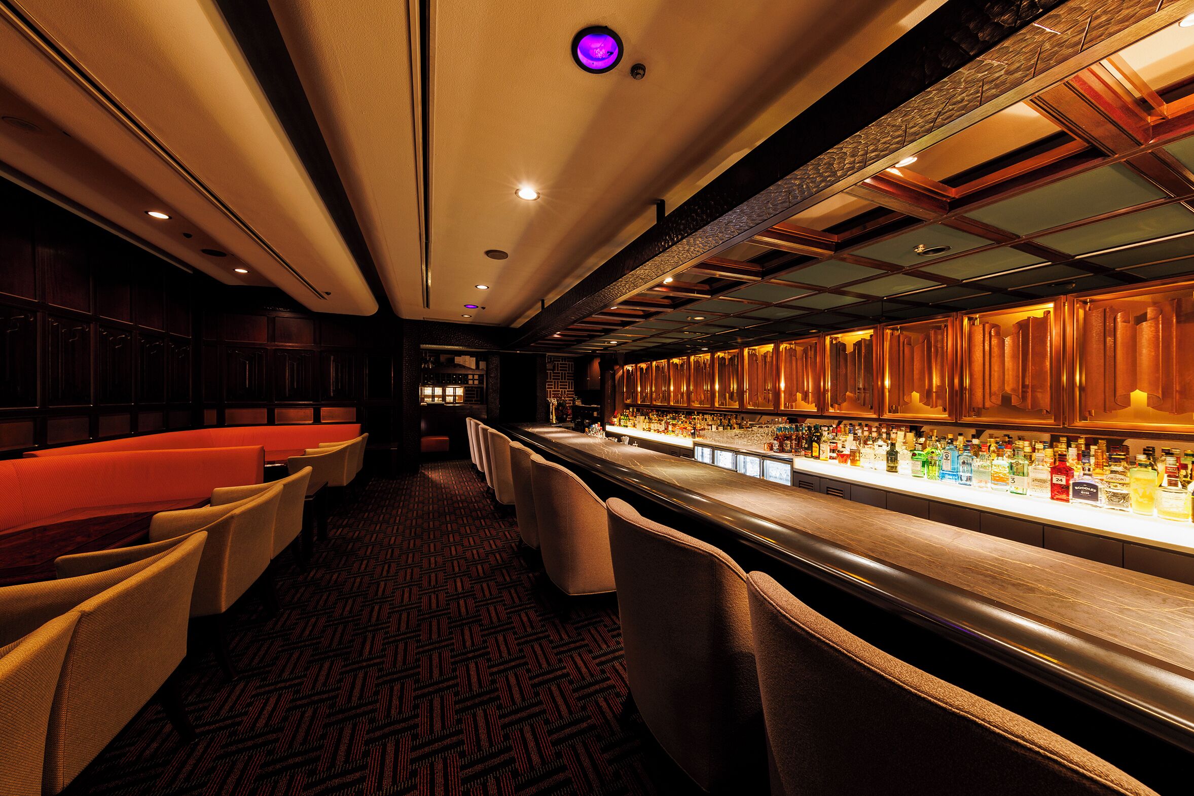 A bar area with a long counter, multiple seating options, and a patterned carpet.