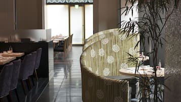 A modern dining area with a long table, chairs, and a sofa. There is a potted plant and a wall with a textured pattern.