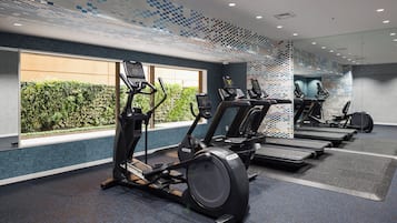 A gym with treadmills, exercise bikes, and a large window with a view of greenery.