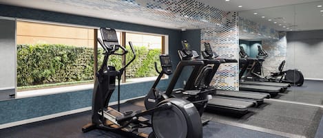 Un gimnasio con cintas de correr, bicicletas estáticas y un ventanal con vistas a zonas verdes.