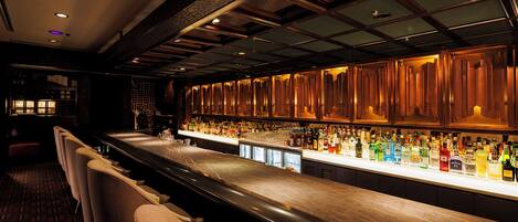 Zona de bar con una barra alargada, diversas opciones de asientos y una gran variedad de botellas y copas.