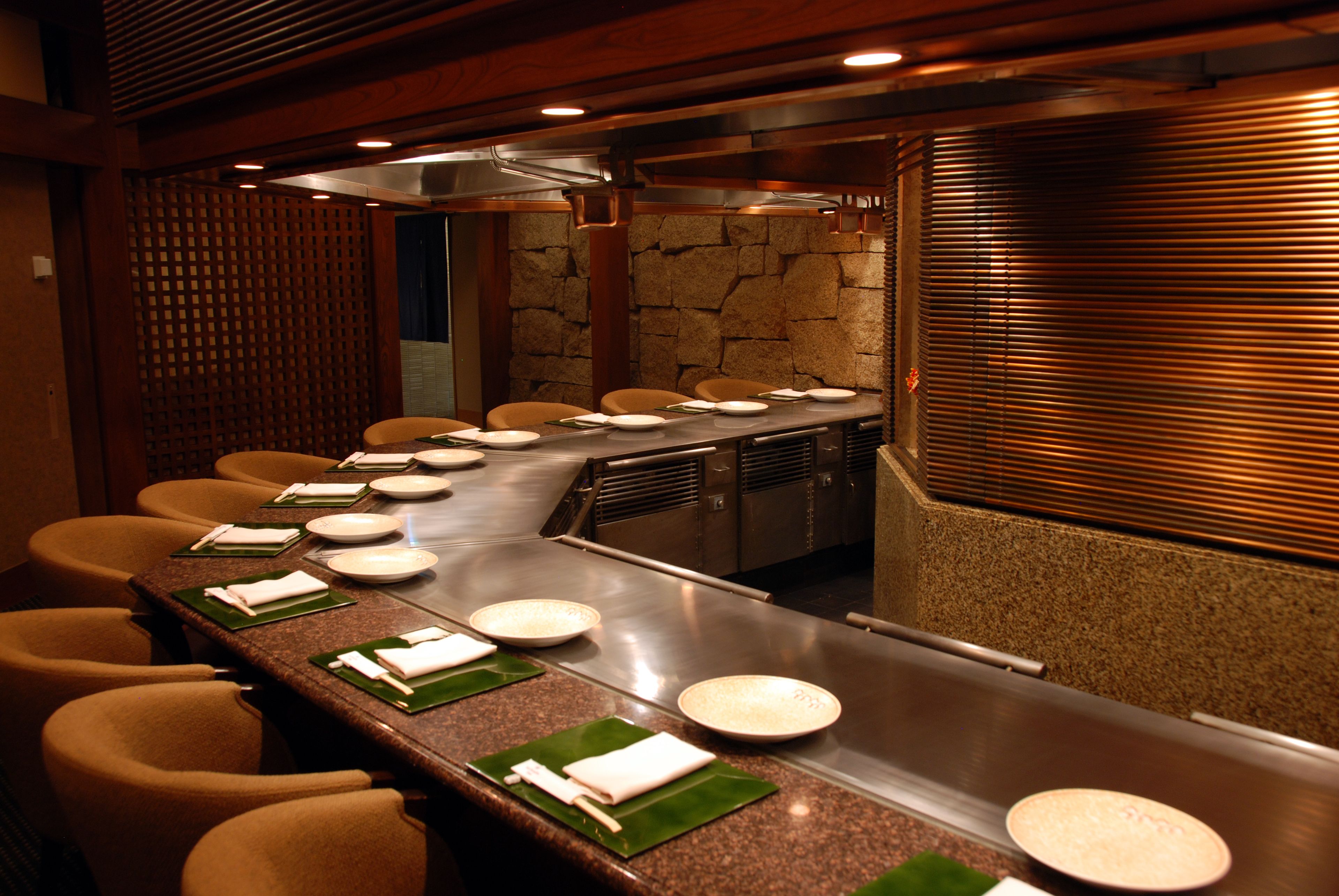 A restaurant with a long counter, multiple chairs, and a stone wall.