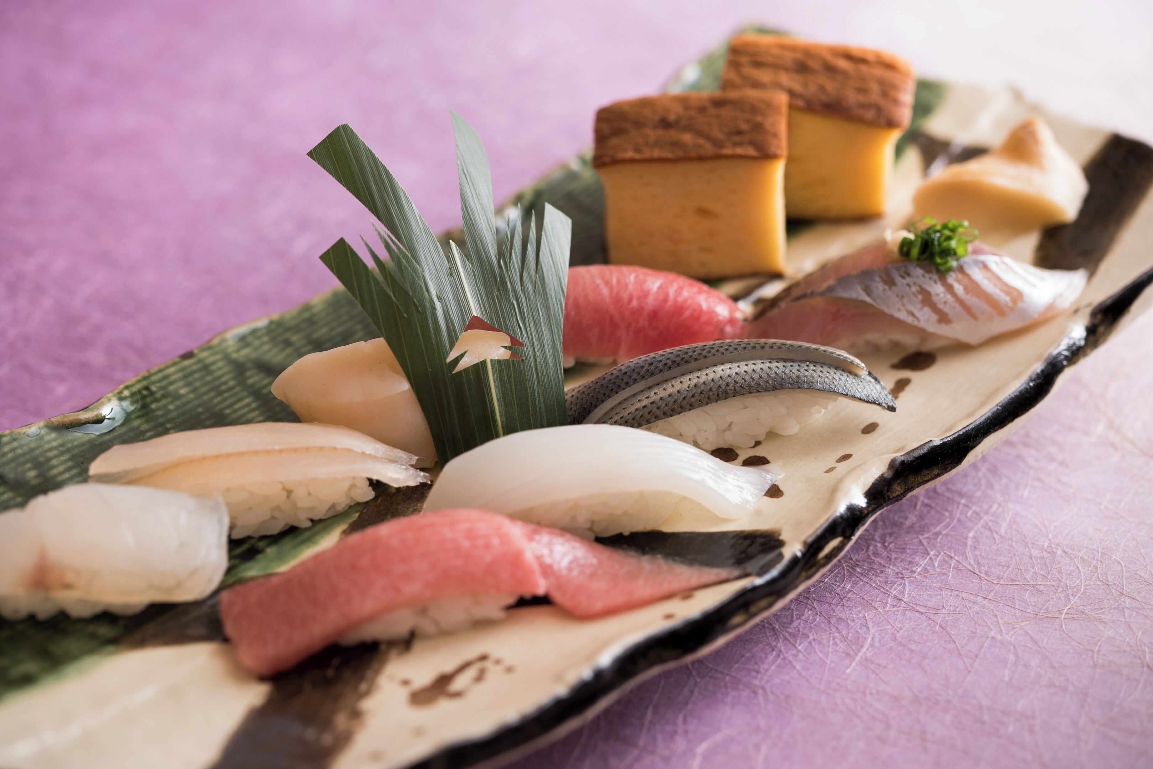 Une variété de sushis présentés sur un plateau en bois, le tout sur un fond violet.