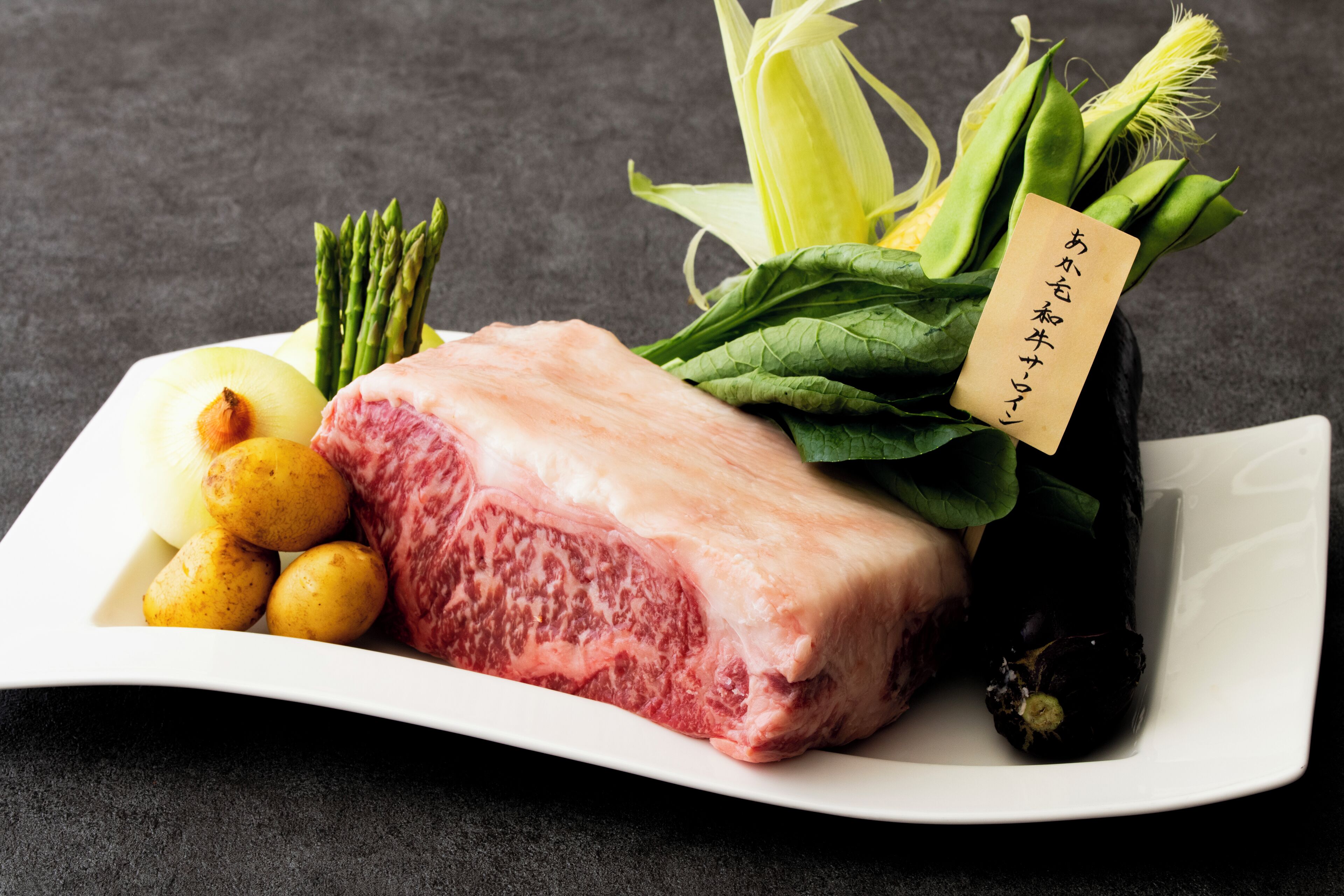 Een bord met vlees, asperges, mais en aardappelen.