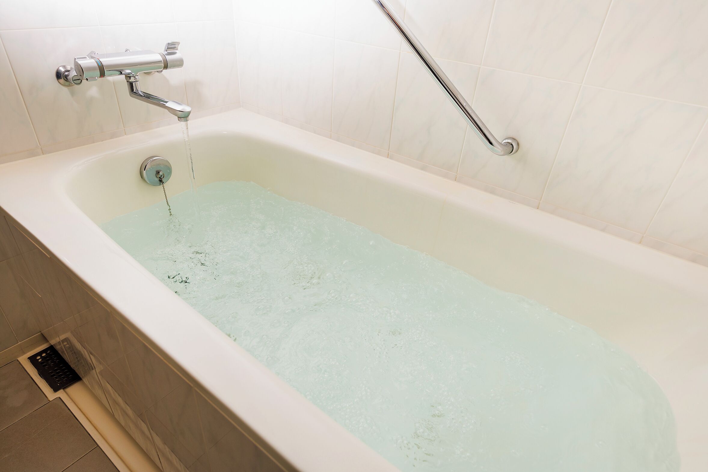 A bathtub with running water, a handheld showerhead, and a grab bar.