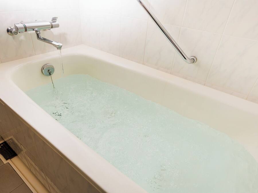 A bathtub with running water, a handheld showerhead, and a grab bar.