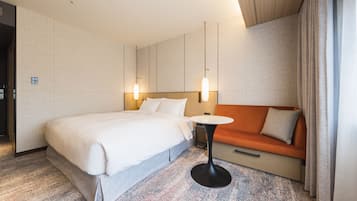A hotel room with a large bed, a small table, an orange sofa, and a modern light fixture.