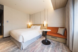 A hotel room with a large bed, a small table, an orange sofa, and a modern light fixture.