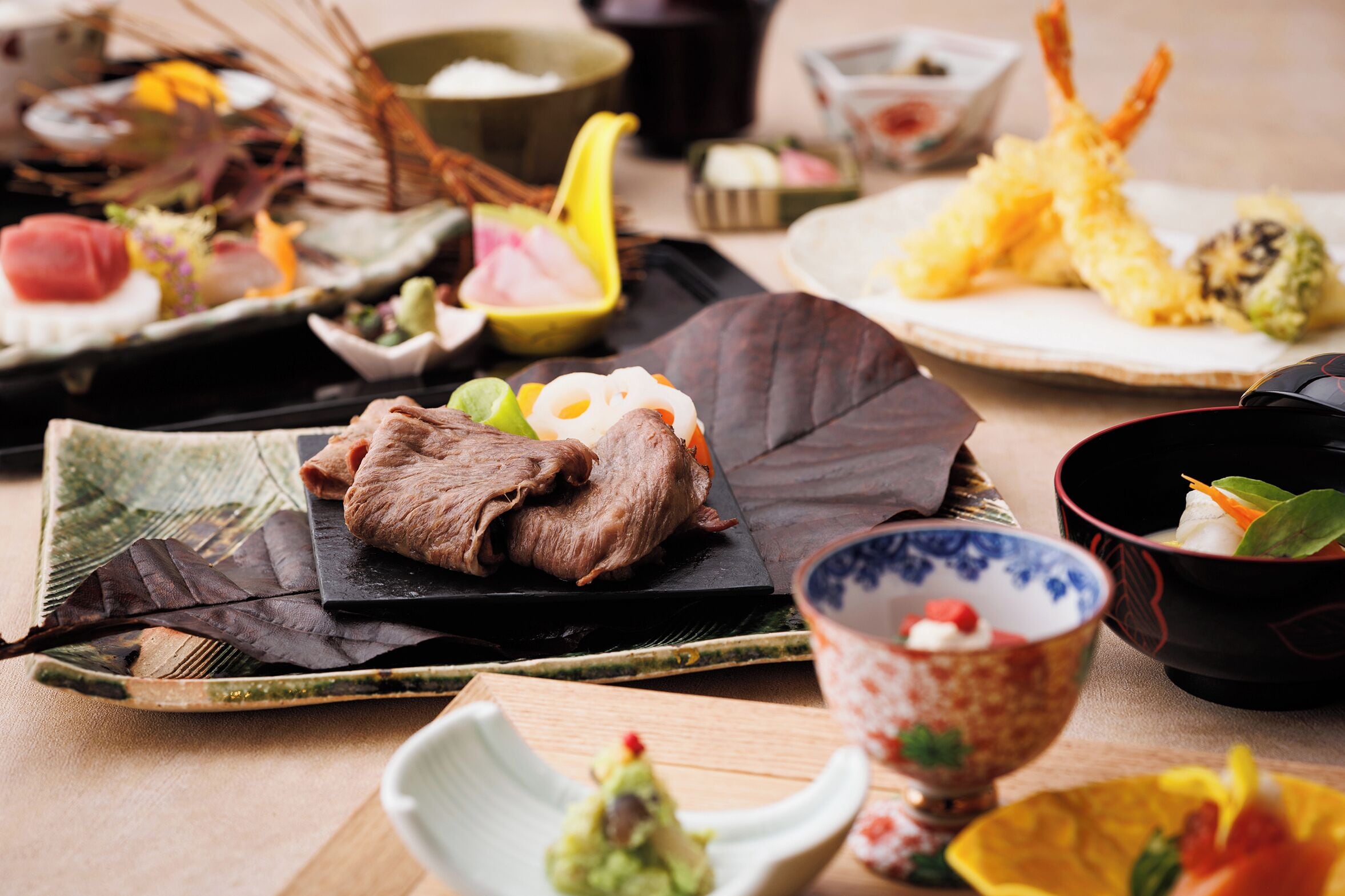 A variety of traditional Japanese dishes on a wooden table, including tempura, sashimi, and a bowl of miso soup.