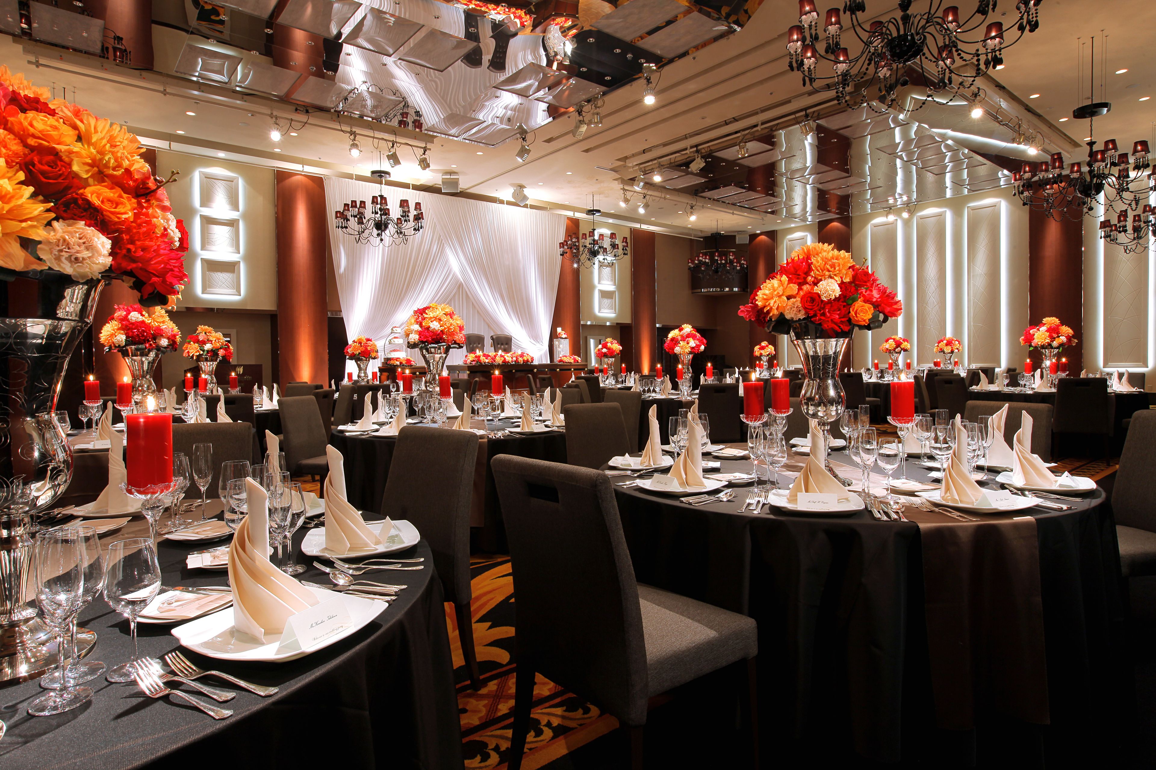 A banquet hall with round tables set for dining, featuring floral centerpieces and red candles.