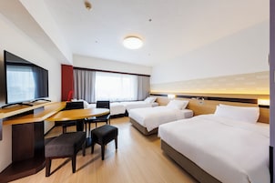 A hotel room with a desk, two beds, a TV, and a window with curtains.