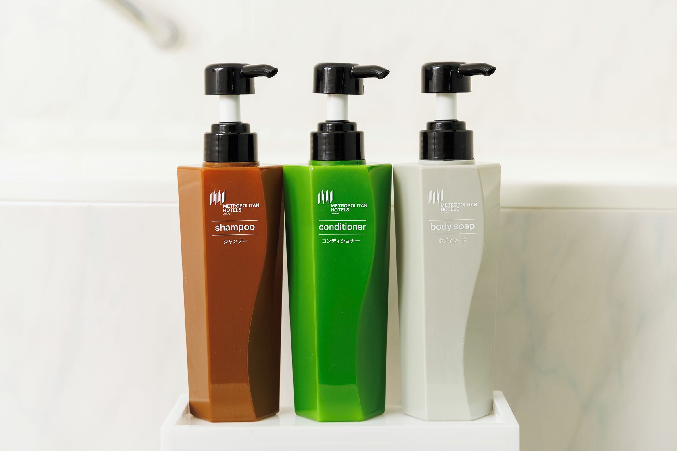 Three bottles of Metropolitan body care products on a white shelf.