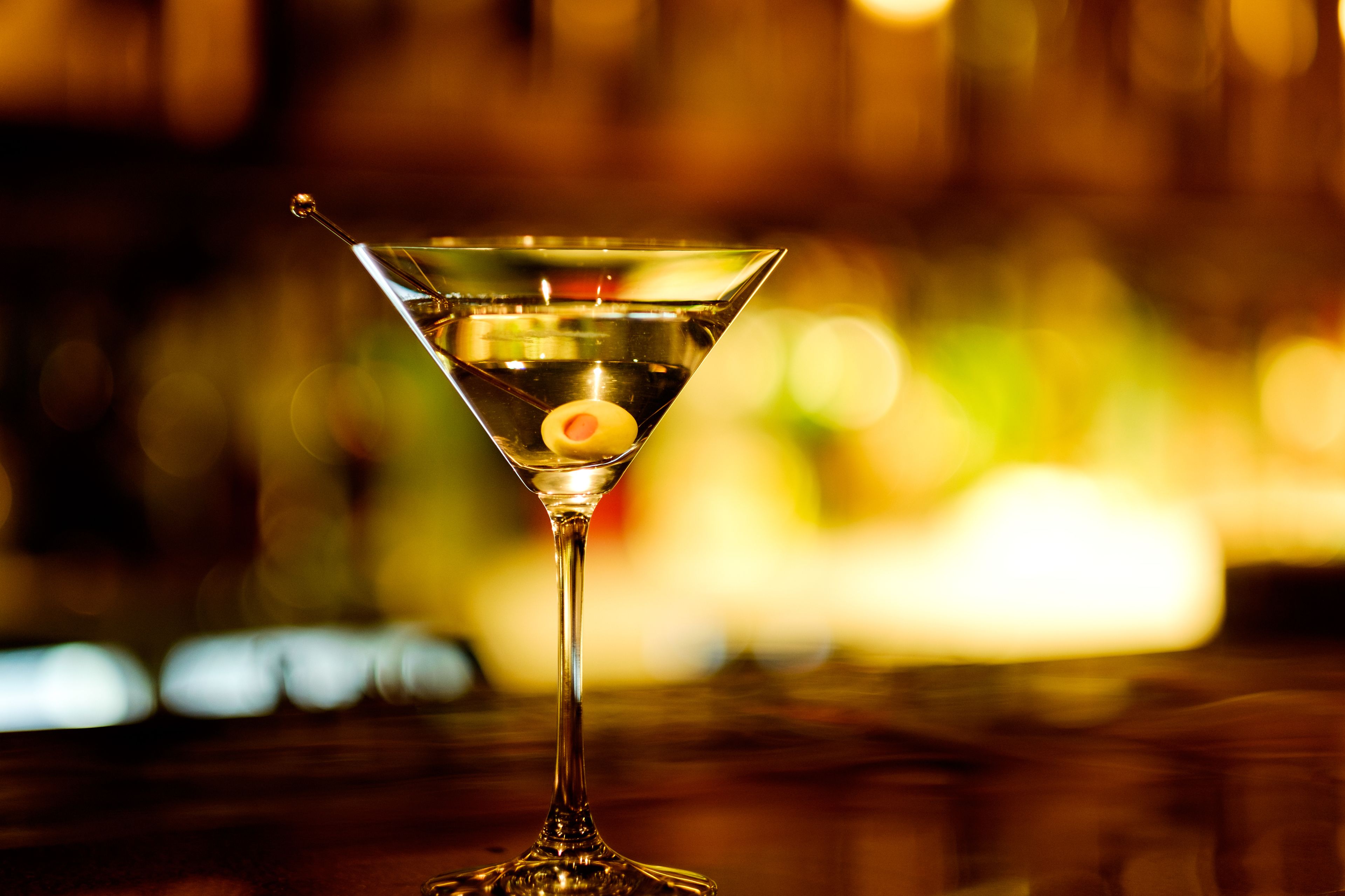 Una copa de martini con aceituna sobre una barra.