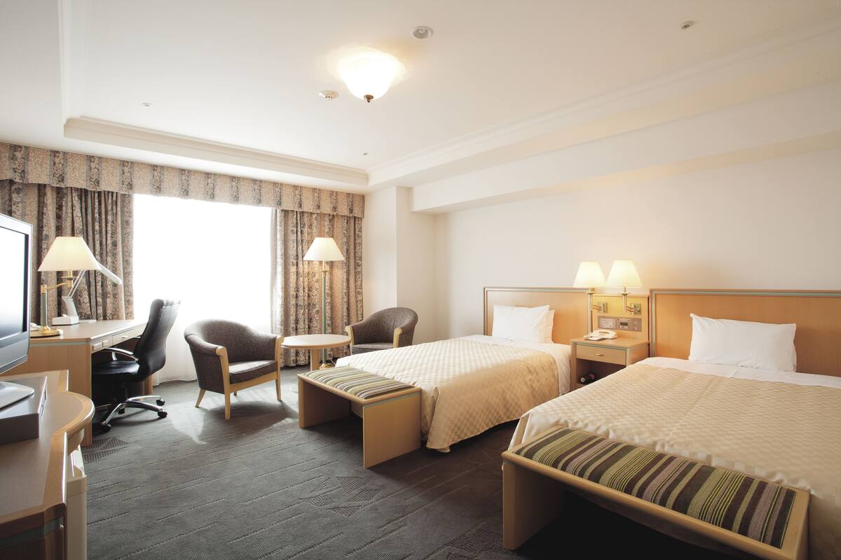 Une chambre d’hôtel avec deux lits, un bureau, une chaise, une petite table et un téléviseur.