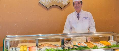 A buffet counter with various seafood dishes, a fan, and a chef in a white uniform.