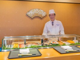 A buffet counter with various seafood dishes, a fan, and a chef in a white uniform.