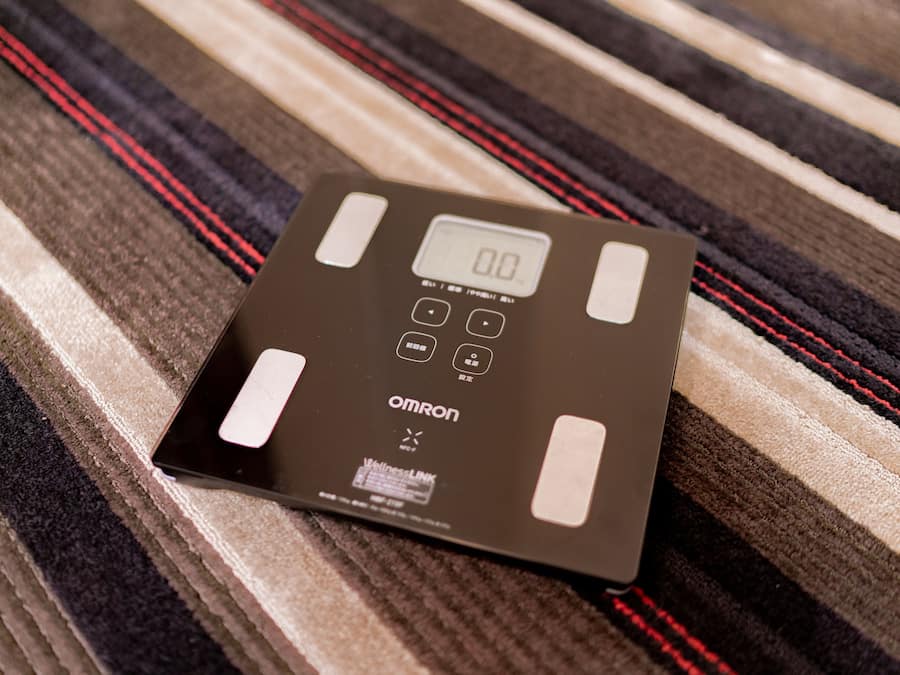 A digital scale with a display and buttons on a striped carpet.
