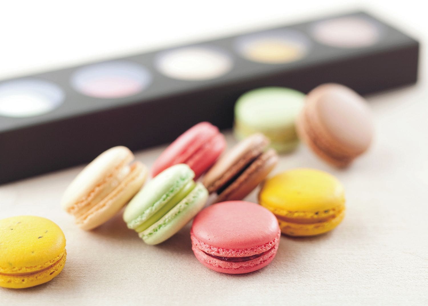A collection of colorful macarons on a surface with a blurred makeup palette in the background.