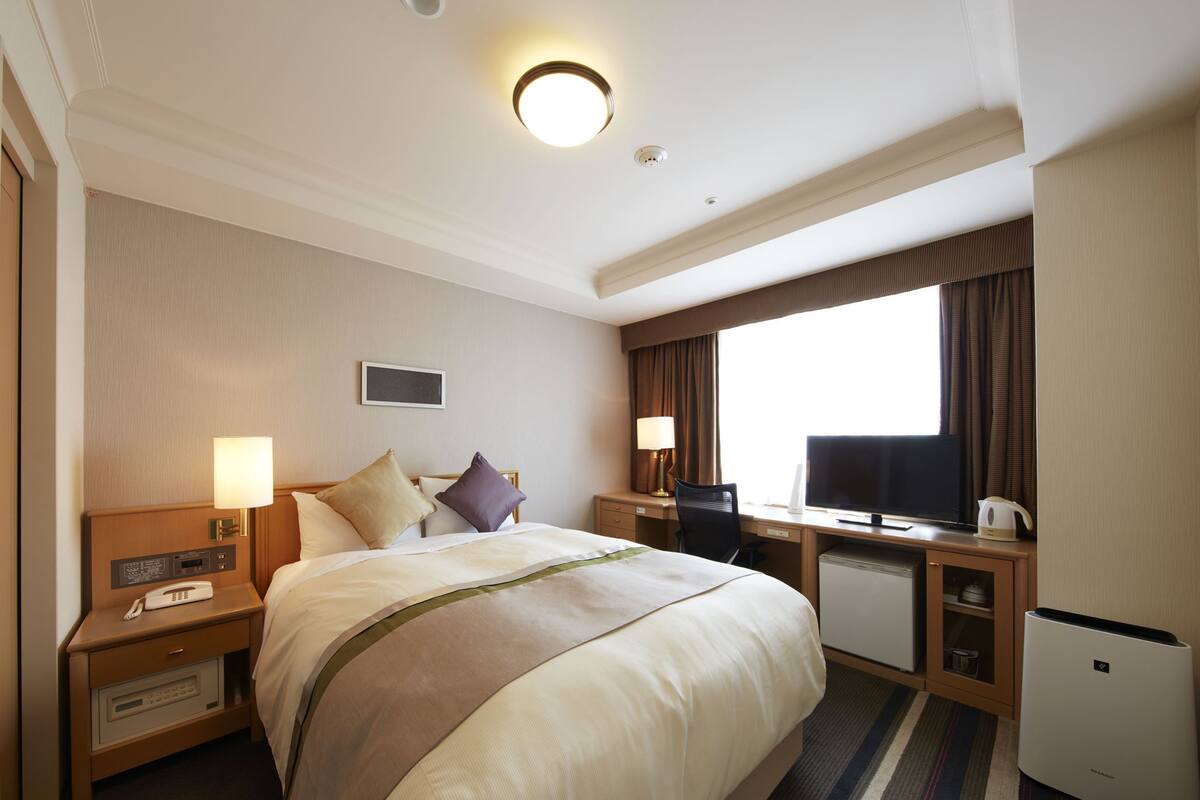 Une chambre d’hôtel avec un grand lit, des tables de chevet avec des lampes, un bureau avec un ordinateur et un mini-bar.