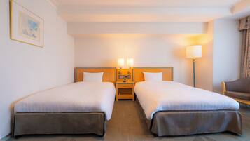 A hotel room with two single beds, a nightstand with a lamp, a chair, and a framed picture on the wall.