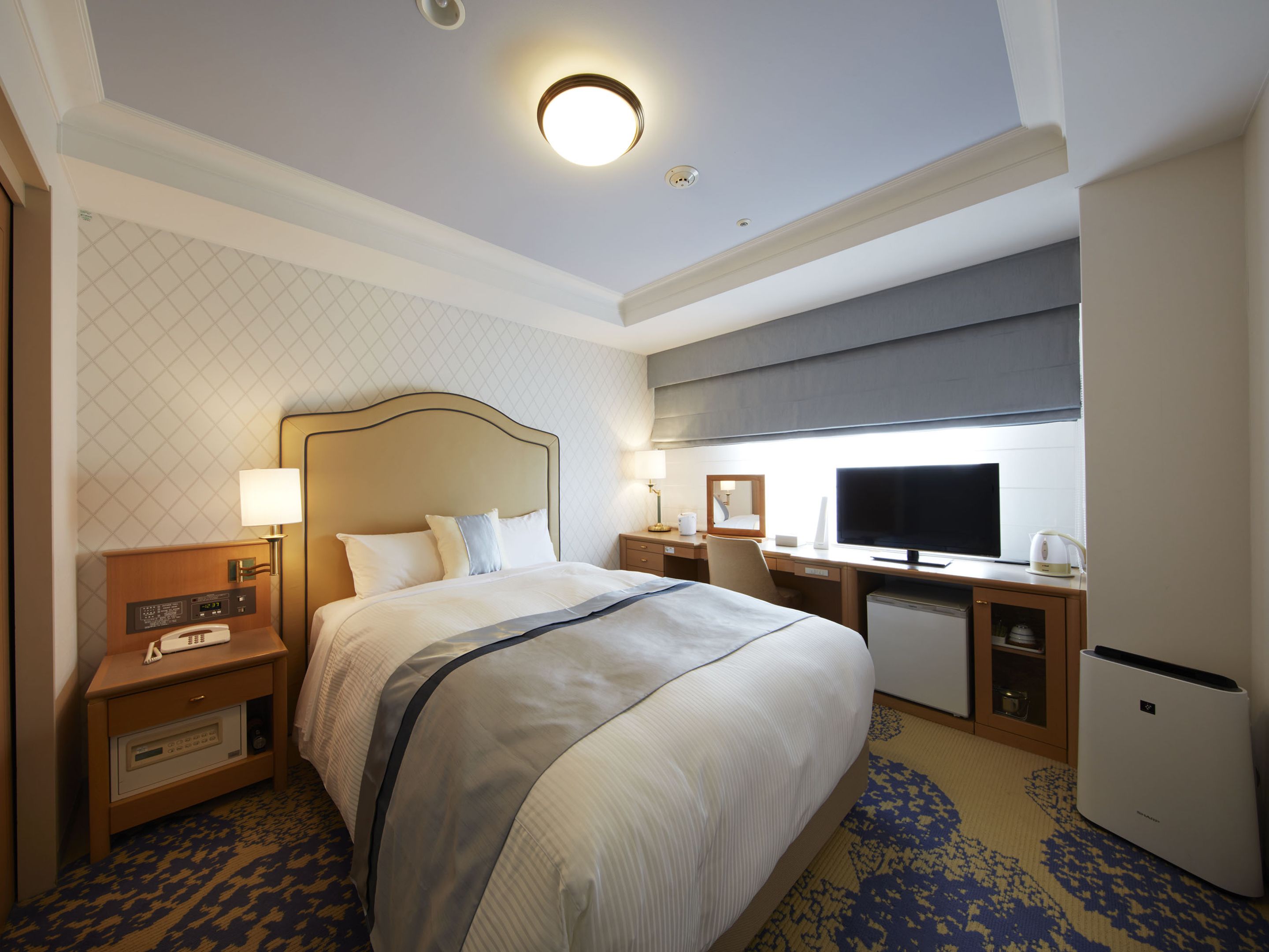 A hotel room with a large bed, a desk with a computer, a television, and a minibar.