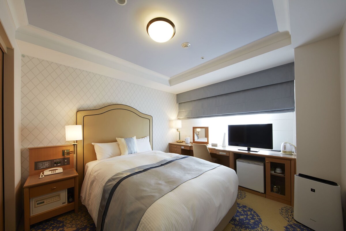 Een hotelkamer met een groot bed, een bureau met een computer, een televisie en een minibar.