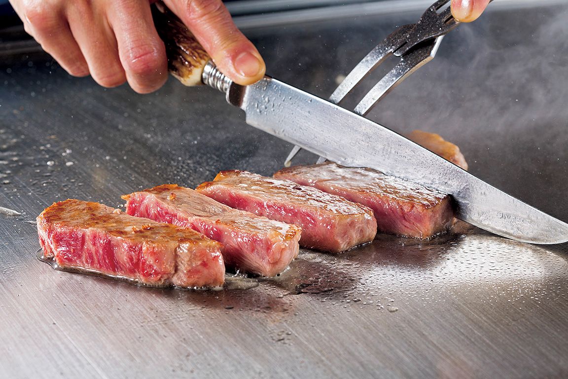 A person slicing a steak on a cutting board.