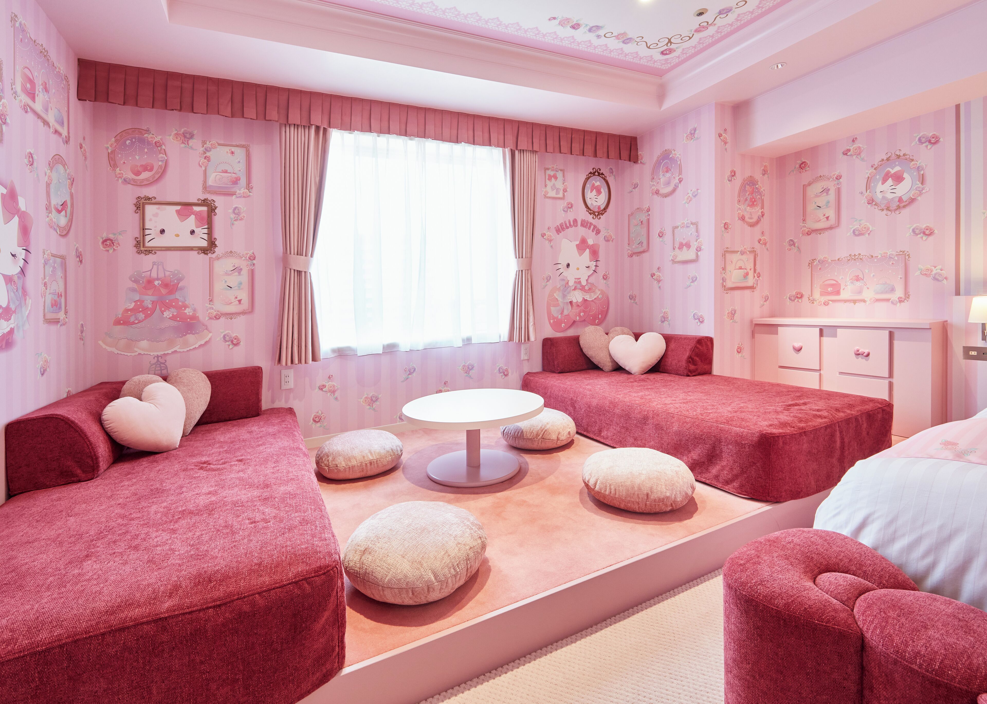 A pink-themed bedroom with two beds, a round table, and heart-shaped pillows.
