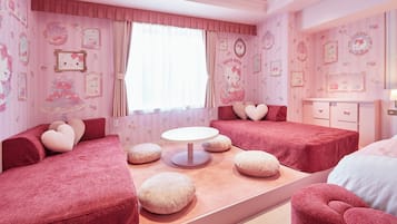 A pink-themed bedroom with two beds, a round table, and heart-shaped pillows.