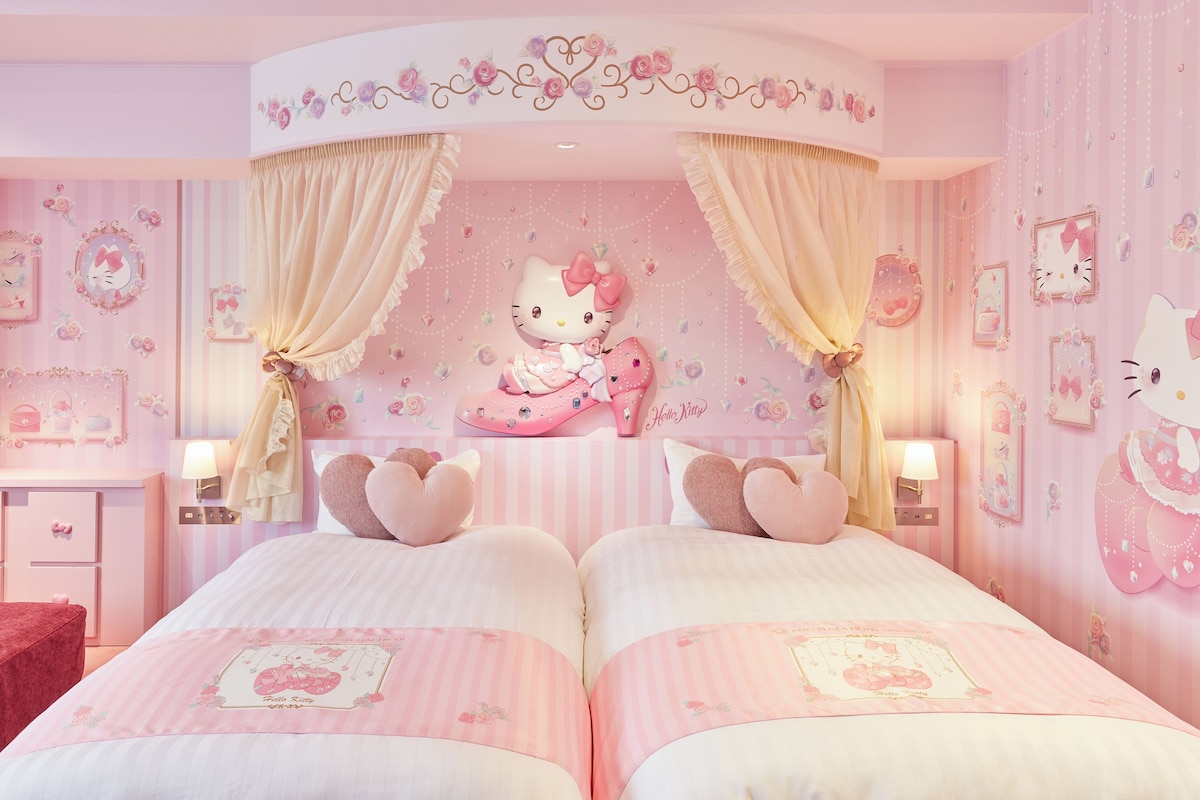 Een roze slaapkamer met twee bedden, Hello Kitty decoraties, en een kaptafel met spiegel.