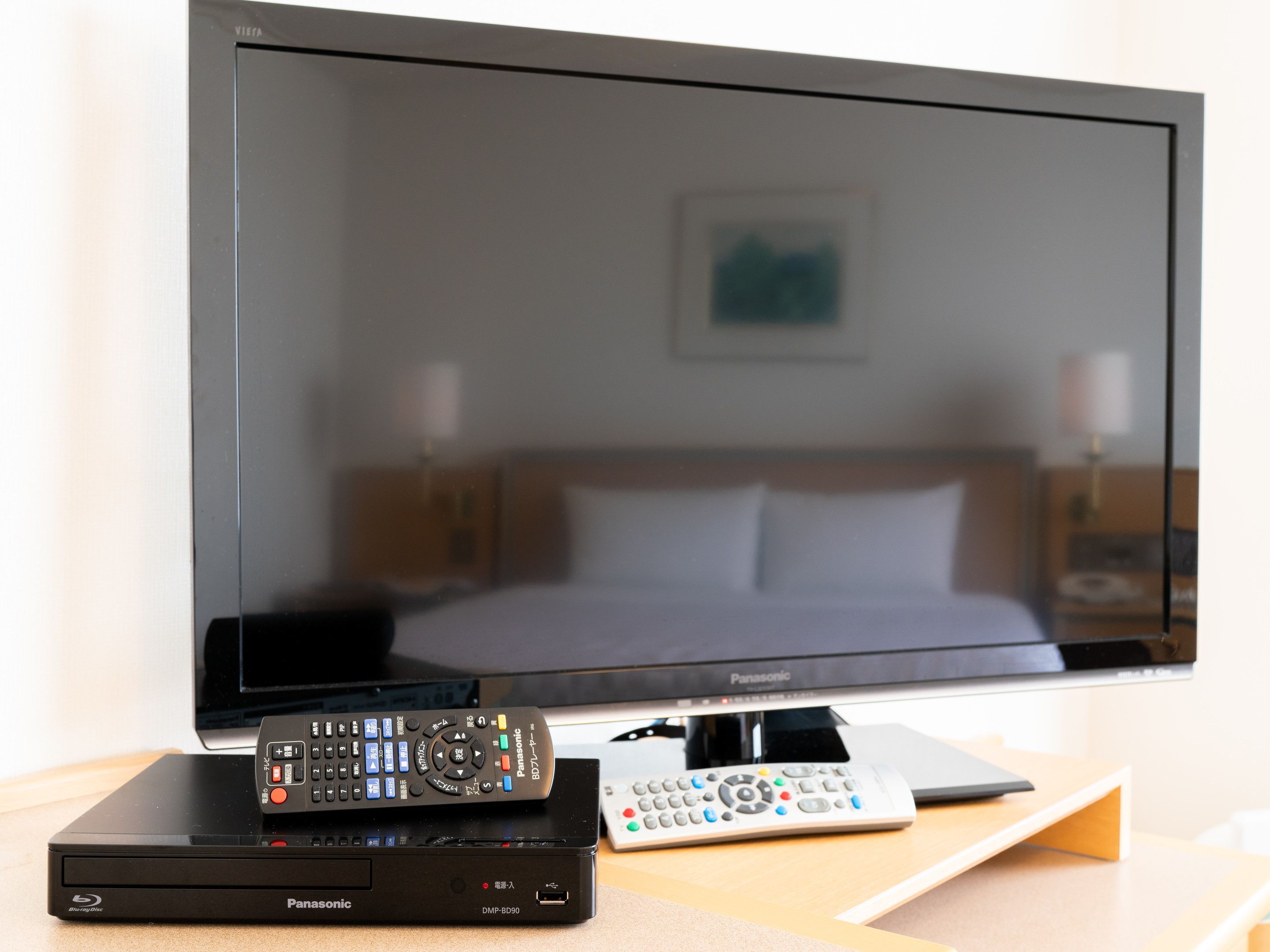 Un lecteur Blu-ray Panasonic DMP-BD90 et une télécommande sont posés sur une table en bois devant un téléviseur.
