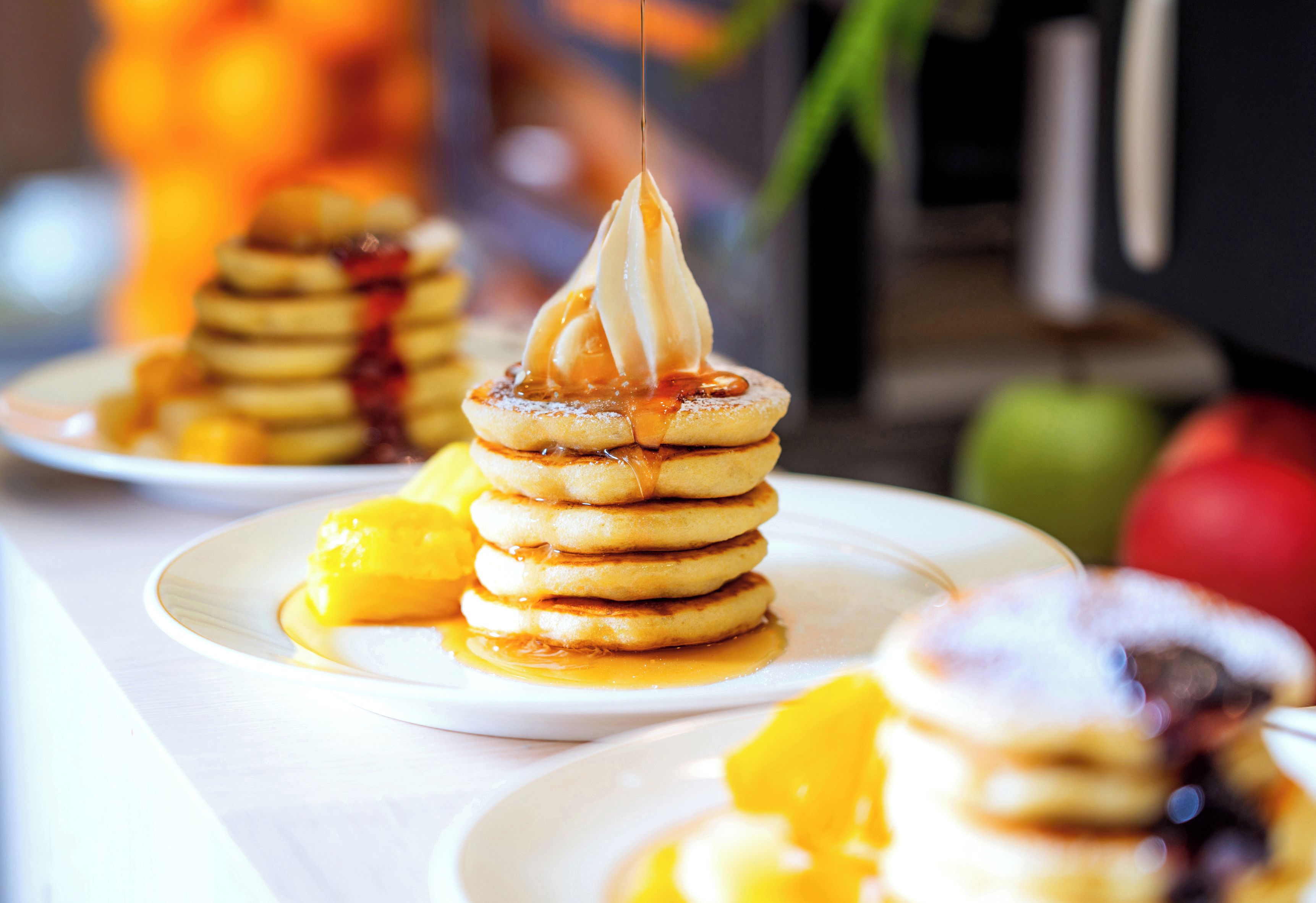 A stack of pancakes with syrup and a dollop of whipped cream on a plate.