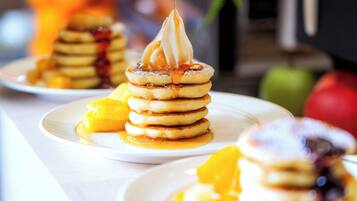 A stack of pancakes with syrup and a dollop of whipped cream on a plate.