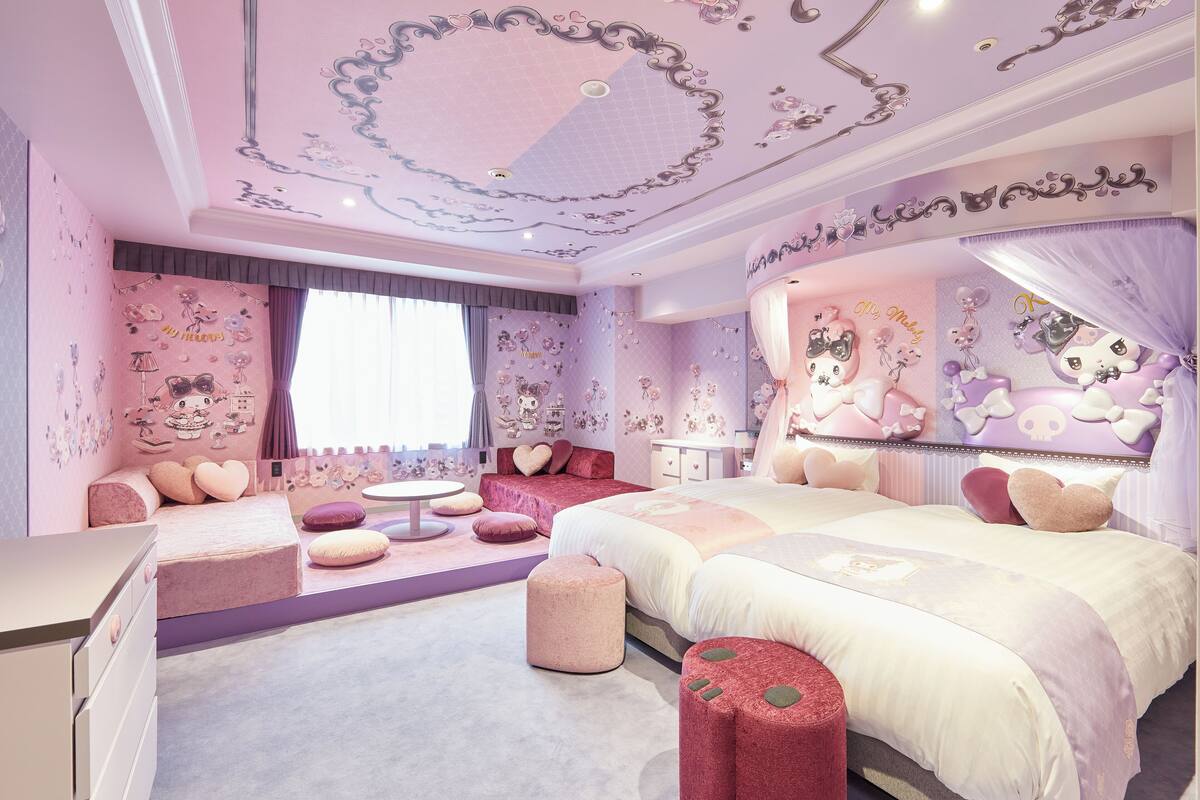 Une chambre à coucher décorée dans des tons roses, avec deux lits, une coiffeuse et un coin salon.
