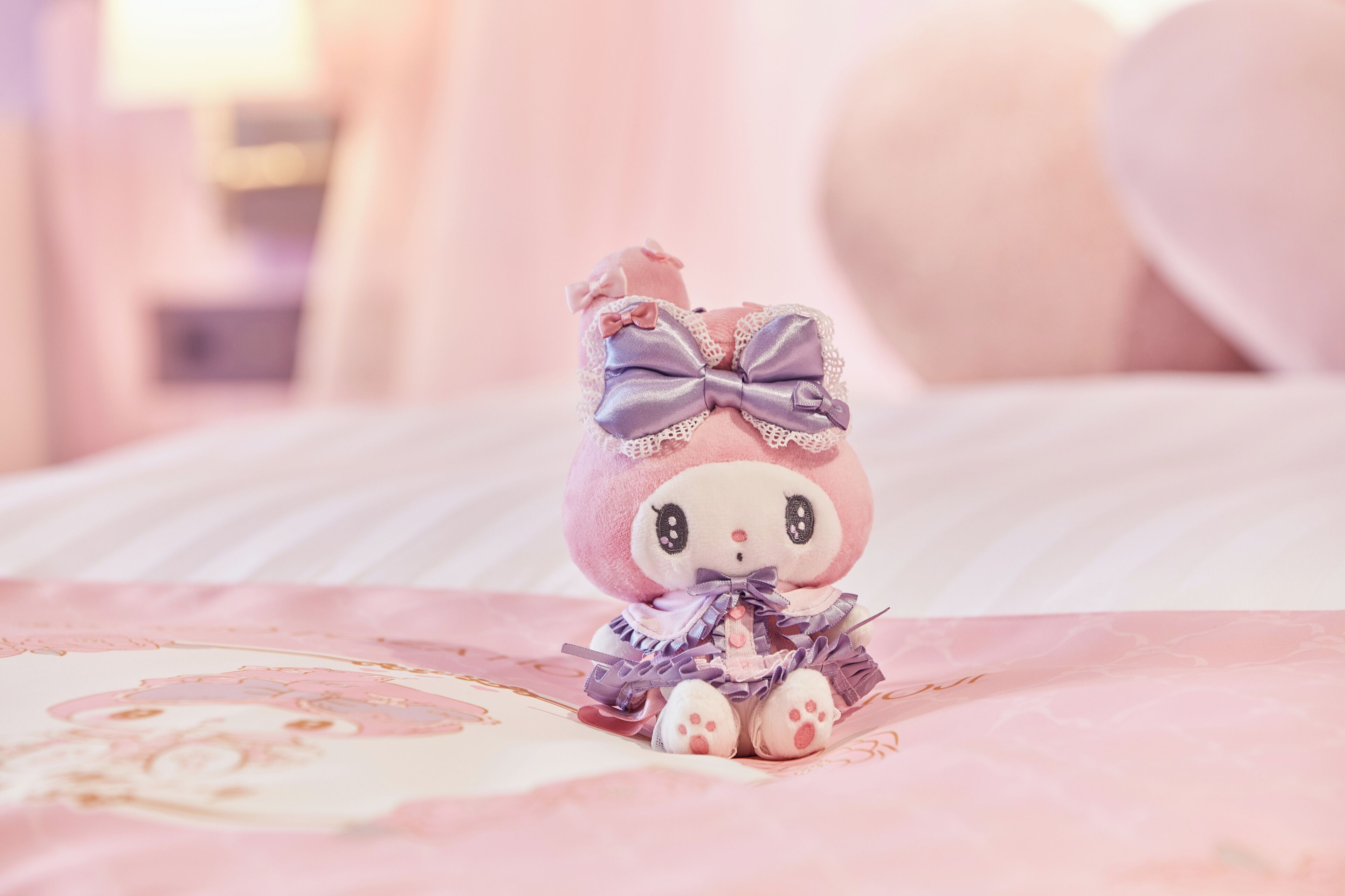 A plush toy on a bed with a pink and white patterned bedspread.