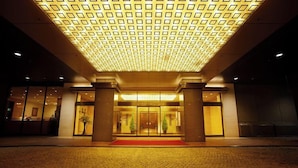 Entrada de un hotel con techo de diseño geométrico, alfombra roja y puertas dobles.