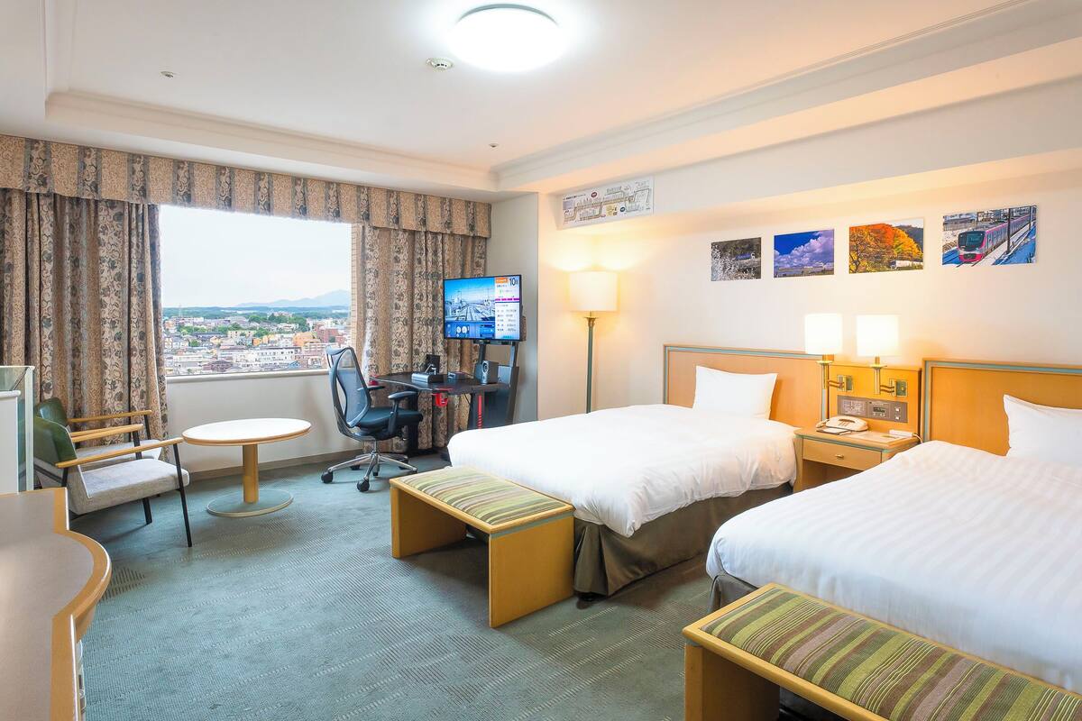 Une chambre d’hôtel avec deux lits, un bureau avec une chaise, une petite table, un téléviseur et une vue sur la ville.