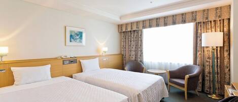 A hotel room with two beds, a chair, a small table, and a window with curtains.