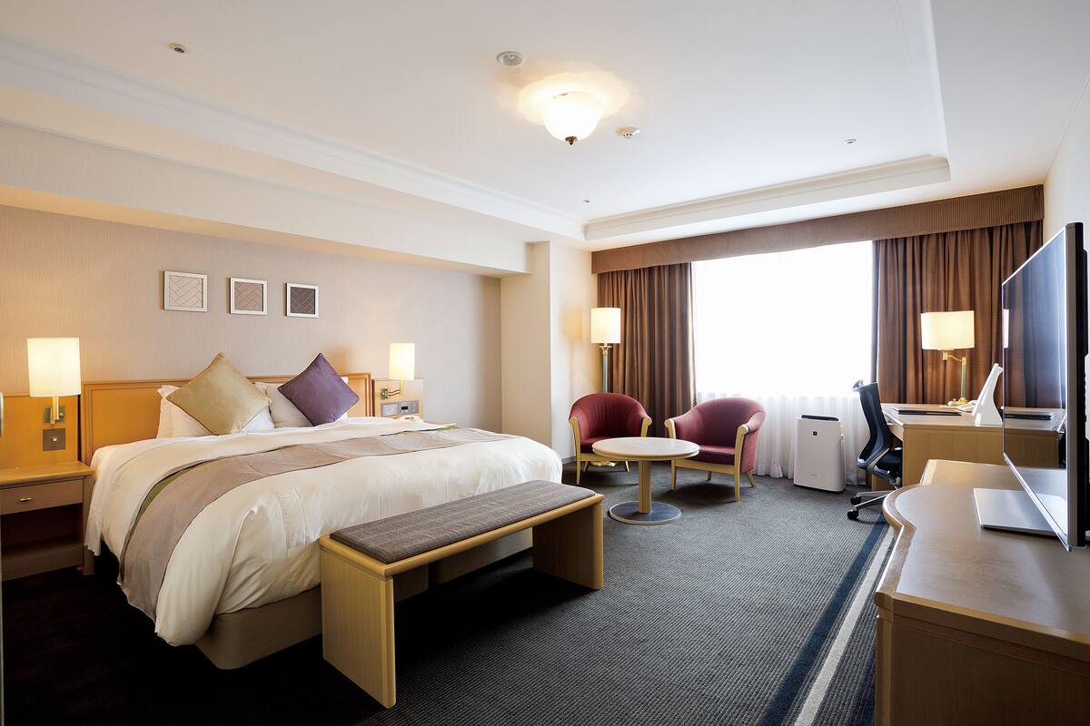 Une chambre d’hôtel avec un grand lit, des tables de chevet, un bureau avec un ordinateur, une chaise et un téléviseur.