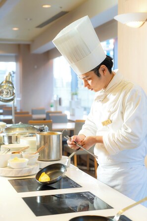 Un chef, vêtu d’une blouse et d’un chapeau blancs, cuisine sur une cuisinière.
