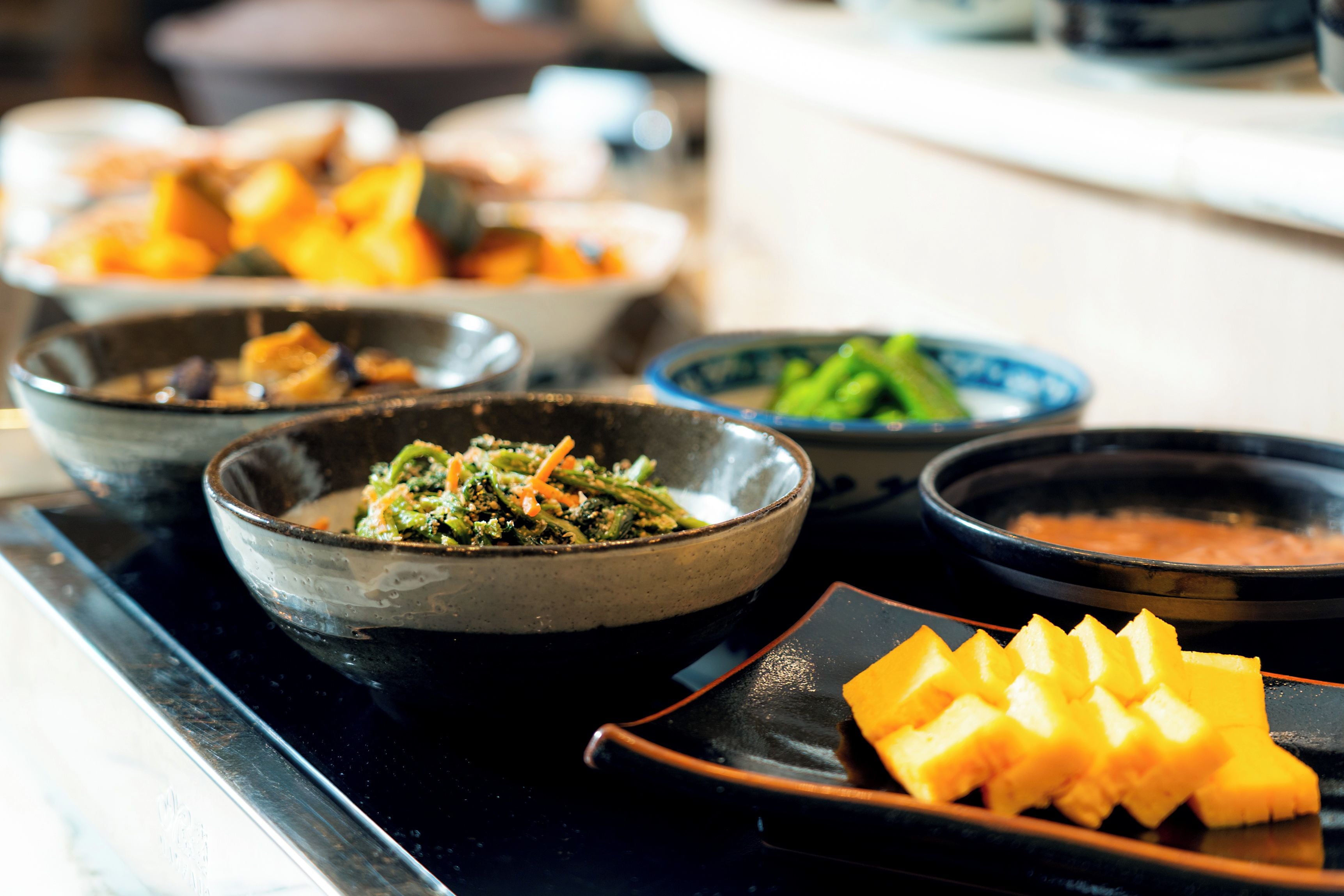 A buffet table with various dishes including a bowl of mixed vegetables, a bowl of soup, and a plate of fruit.