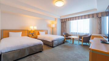 A hotel room with two beds, a desk, a chair, a small table, and a television.